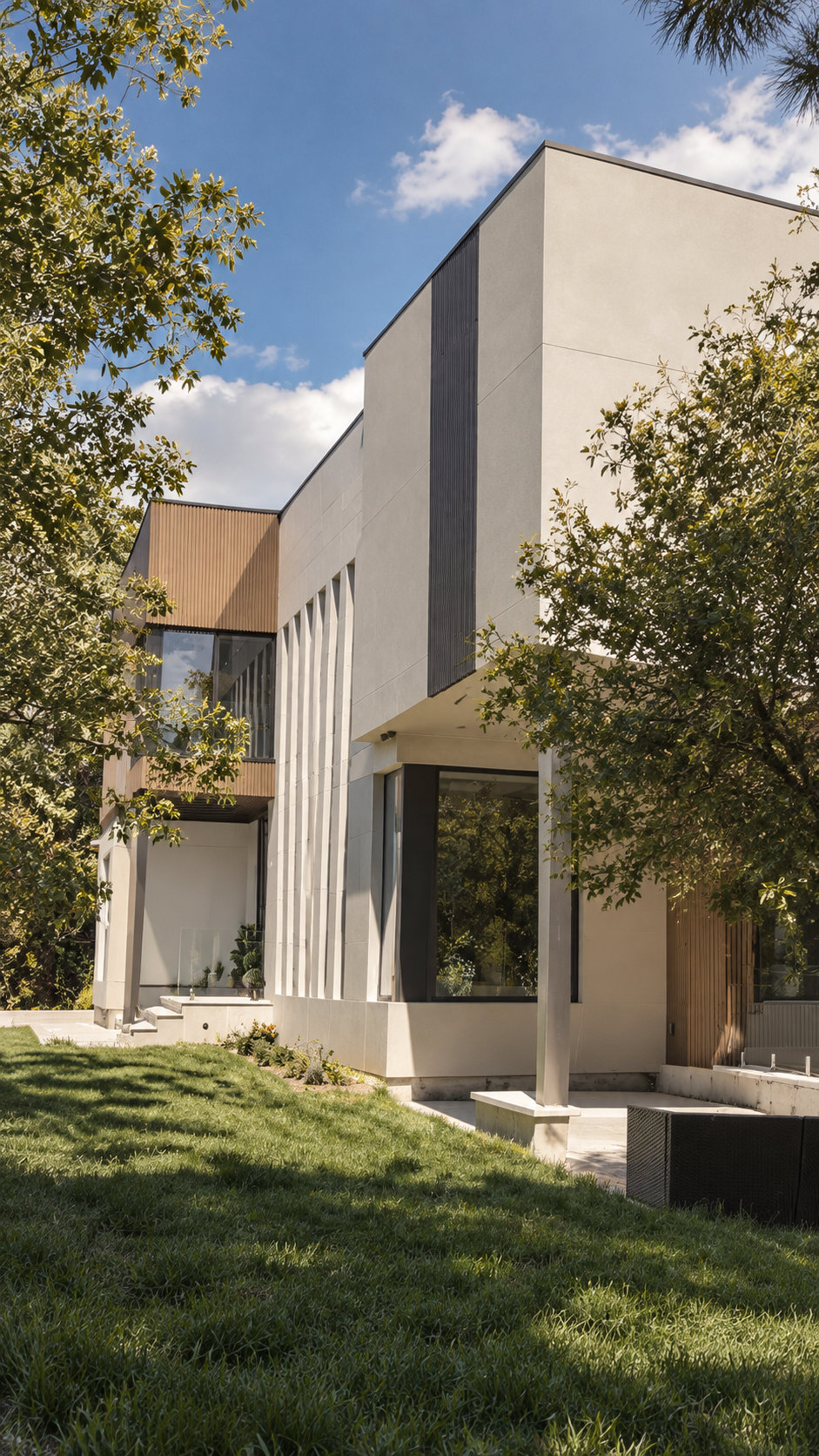 Portrait view of dramatic white contemporary home with glass walls surrounded by trees
